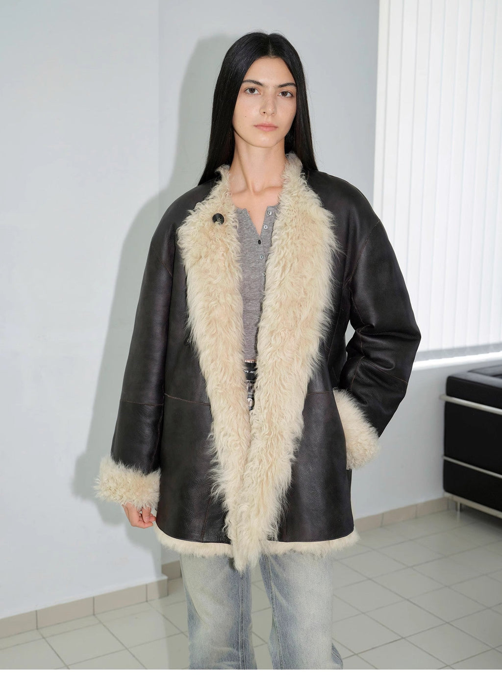 Person wearing a black leather coat with white fur trim indoors.